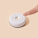 White circular light with a hand pressing on it against a beige background