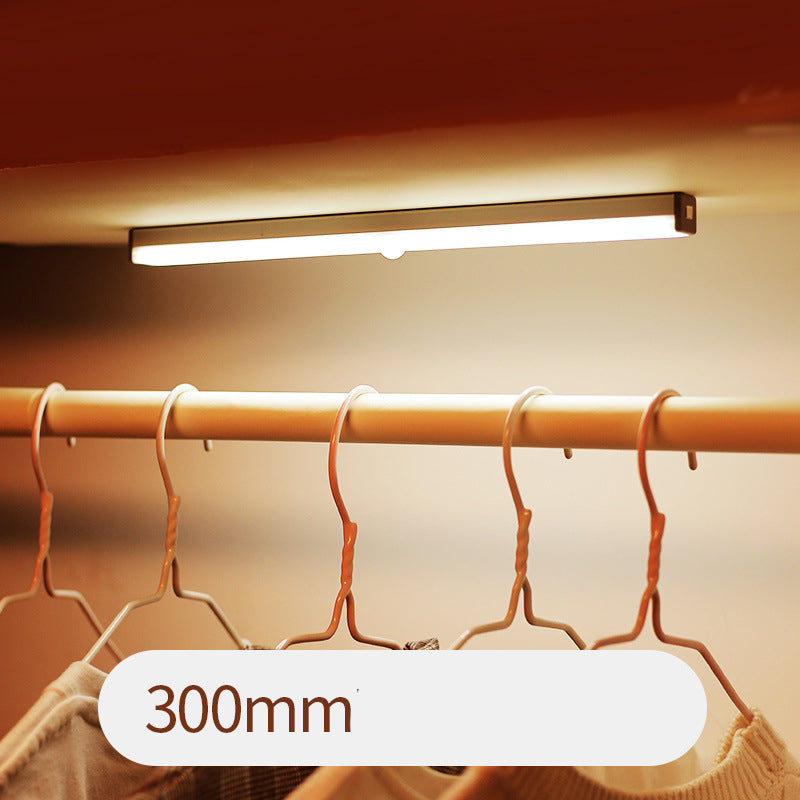 Under-cabinet light fixture above a clothing rack with hangers.