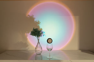 Vase with flowers and a glass on a reflective surface with a colorful circular light projection on the wall.